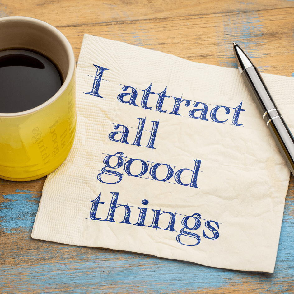Notebook on a wooden table with the words ‘I attract all good things’, next to a yellow cup and pen – symbolising positivity and mindfulness.